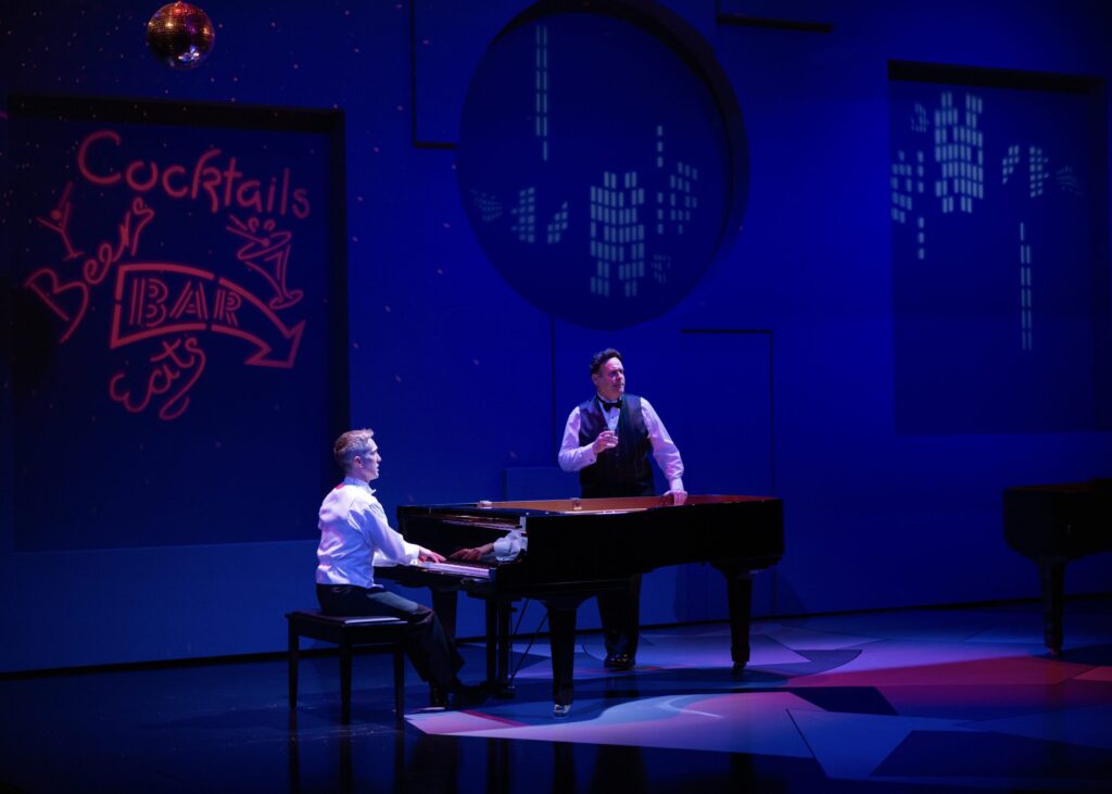 The image depicts a stage scene with two individuals, each dressed formally. One person, wearing a white shirt, sits at a grand piano on the left, playing. On the right, another person in a vest and bow tie stands beside the piano, holding a glass, suggesting a performance or a theatrical setting. The background is deep blue with a disco ball hanging above, casting scattered light across the scene. On the left wall, red neon-style signage reads "Cocktails," "Beer," "BAR," and "eats," with illustrations of an arrow and a martini glass. On the right side, a circular window shows a stylized city skyline pattern in light blue.
